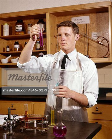 1960s COLLEGE STUDENT IN CHEMISTRY LABORATORY LOOKING AT SOLUTION IN BEAKER