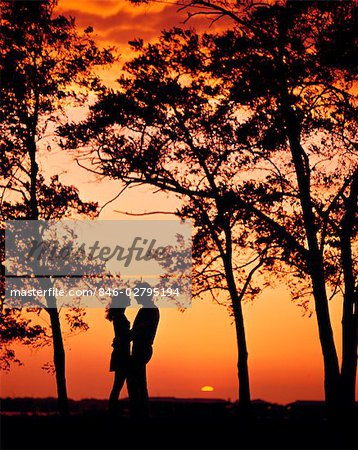 1970s SILHOUETTED COUPLE MAN WOMAN AT SUNSET WITH TREES STANDING FACE TO FACE ROMANTIC MOODY