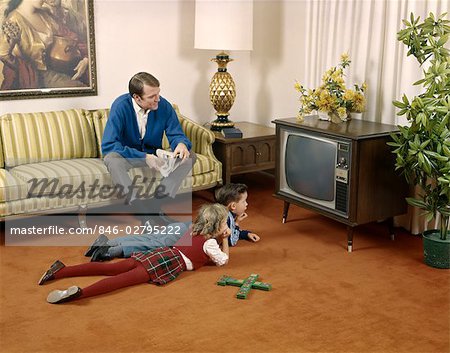 1960s FAMILY MAN FATHER SITTING ON LIVING ROOM COUCH WITH BOY SON AND GIRL DAUGHTER LYING ON FLOOR WATCHING TELEVISION TOGETHER