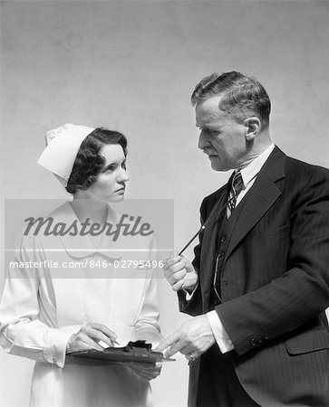 1930s DOCTOR IN SUIT AND NECKTIE CONFERS WITH NURSE IN UNIFORM AND CAP HOLDING CLIPBOARD CHART