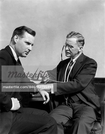 1930s MAN DOCTOR TAKING PULSE OF MAN PATIENT
