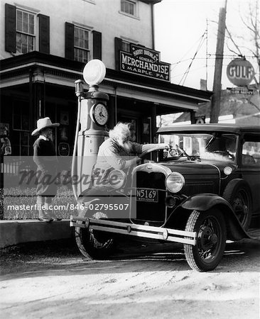 ELDERLY GRANDFATHER FILLING UP FORD CAR IN FRONT OF PENNSYLVANIA GENERAL STORE WITH GRANDSON WATCHING 1930s