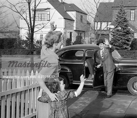 1950s MOTHER AND DAUGHTER WAVING TO FATHER OPENING AUTOMOBILE DOOR IN FRONT OF SUBURBAN HOME