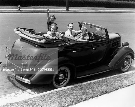 1940s FAMILY OF FOUR IN CONVERTIBLE FORD V-8 SEDAN SMILING AT CAMERA