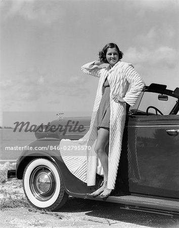 1930s 1940s SMILING WOMAN WEARING CHENILLE BEACH ROBE POSING ON RUNNING BOARD OF CONVERTIBLE ROADSTER AUTOMOBILE