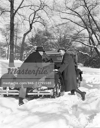 1930s TWO MEN LOOKING UNDER HOOD OF CAR WINTER SNOWY STREET BROKEN REPAIR COLD DISCUSSION CONSULTATION PROBLEM