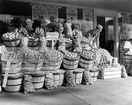 ANNÉES 1940 ÉPICIER DANS CAP & TABLIER BLANC EXPOSANT FRUITS SUR TROTTOIR EN FACE DU SUPERMARCHÉ