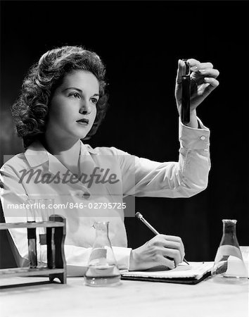 1940s STUDENT NURSE HOLDING UP TEST TUBE WHILE TAKING NOTES IN SCIENCE CLASS