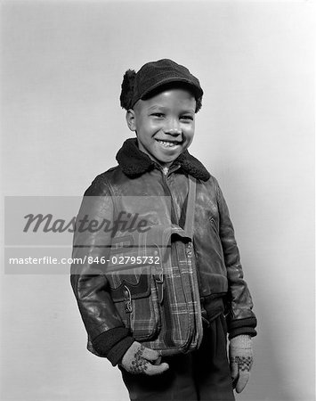 1940s 1950s AFRICAN AMERICAN BOY SMILING WEARING WINTER JACKET GLOVES HOLDING SCHOOL BOOK BAG