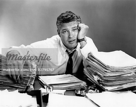 1950s PORTRAIT MAN OVERWORKED WITH DESK FULL OF PAPERS