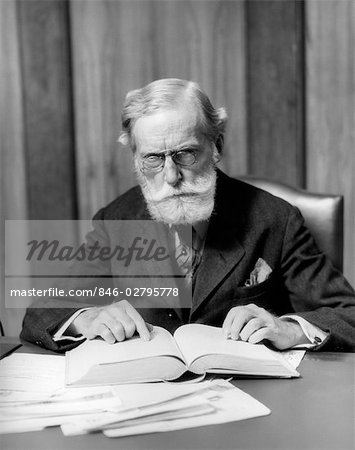 1930s ELDER MAN IN GLASSES SITTING AT DESK READING BOOK