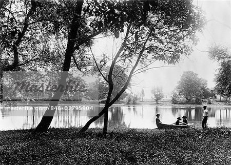 1890s 1900s TURN OF THE CENTURY OLDER BROTHER WATCHING GROUP OF THREE YOUNGER CHILDREN IN ROWBOAT ON SMALL LAKE