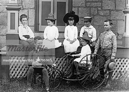 1890s 1900s TURN OF THE CENTURY GROUP OF SEVEN CHILDREN SITTING ON & AROUND PORCH ONE GIRL ON OLD FASHIONED TRICYCLE