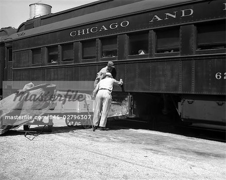 1930s 1940s TWO RAILROAD WORKERS PUTTING CAKES OF ICE INTO CLIMATE CONTROL AIR CONDITIONING COMPARTMENTS OF PASSENGER RAILROAD TRAIN