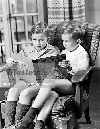 1950s TWO BOYS SITTING IN ONE CHAIR SHARING LARGE BOOK ARMCHAIR