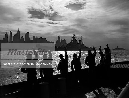 1950s SILHOUETTED SAILORS DECK OF SHIP WAVING SALUTE TO PASSING USN BATTLESHIP AT NIGHT AGAINST NEW YORK CITY SKYLINE