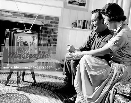 1950s COUPLE HUSBAND AND WIFE WATCHING TV IN LIVING ROOM SMILING INDOOR