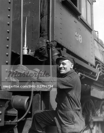 1930s RAILROAD WORKER IN COVERALLS HAT GOGGLES & GLOVES CLIMBING UP ONTO TRAIN