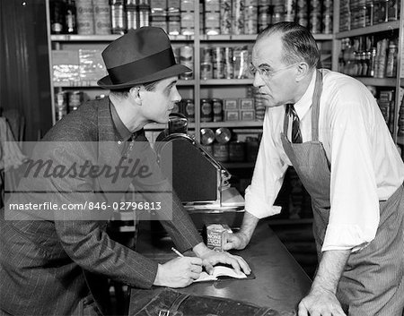 1940s SALESMAN TAKING AN ORDER FROM A GROCER WITH PAD & PENCIL ON THE COUNTER TOP HE'S DRESSED IN SUIT