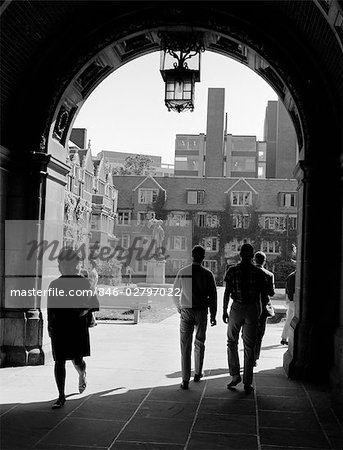 1960s COLLEGE STUDENTS WALKING THROUGH ARCHWAY IN CAMPUS BUILDING WITH QUADRANGLE IN BACKGROUND