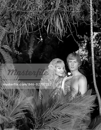 1970s BLOND COUPLE POSED AS ADAM & EVE STANDING NAKED BEHIND TROPICAL FOLIAGE EVE HOLDING APPLE WITH BITE TAKEN OUT