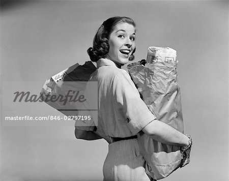 1950s SMILING WOMAN CARRYING GROCERY BAGS BOTH HANDS LOOKING BACK OVER SHOULDER