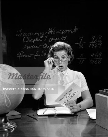 1950s SCHOOL TEACHER AT DESK HAND TO GLASSES EXPRESSION OF SURPRISE OPENING A VALENTINE FOR TEACHER GLOBE BLACKBOARD