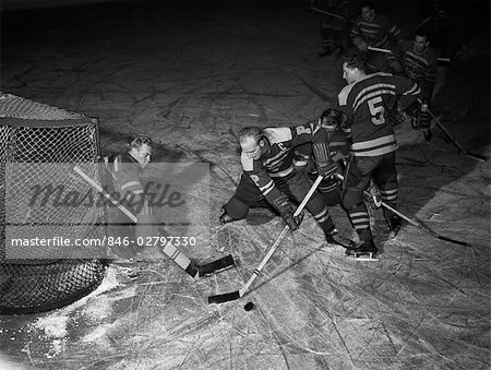 1940s 1950s ICE HOCKEY GAME GOALIE PROTECTING CAGE AS 2 OTHER PLAYERS TRY TO CONTROL PUCK WITH HOCKEY STICKS WINTER SPORT