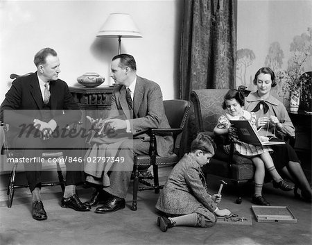 1930s FAMILY IN LIVING ROOM MOTHER KNITS DAUGHTER ON HER LAP WITH BOOK SON ON FLOOR WITH HAMMER