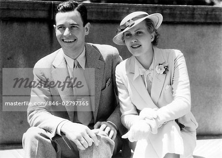 1930s SMILING COUPLE SITTING OUTDOORS IN THE SUNLIGHT