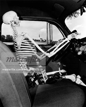 1930s 1940s STILL LIFE OF SKELETON DRIVING CAR WITH WHISKEY BOTTLE AND WOMAN'S SHOES ON SEAT BESIDE IT