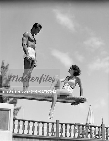 1930s COUPLE BY SWIMMING POOL ON DIVING BOARD TALKING