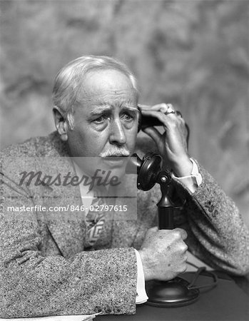 1920s 1930s ELDERLY CONCERNED WORRIED MAN TALKING ON CANDLESTICK PHONE BUSINESS MAN TWEED SUIT SERIOUS EXPRESSION