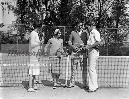 1920s COUPLES DOUBLES TENNIS TWO GIRLS TWO BOYS HOLDING RACKETS STANDING NEAR NET ON TENNIS COURT