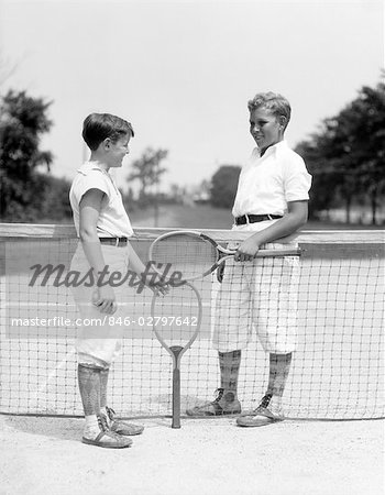 1920s 1930s TWO BOYS TENNIS MATCH HOLDING RACKETS STANDING NEAR NET ON TENNIS COURT