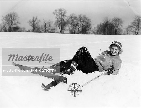 1940ER JAHRE LÄCHELND FRAU SKI KLEIDUNG UND MÜTZE VERLEGUNG IN SCHNEE MIT SKIER UND STÖCKE FALLEN GEFALLENEN UNFALL ANFÄNGER