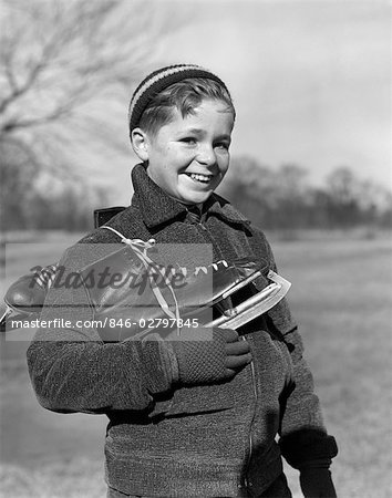 ANNÉES 1930 JEUNE GARÇON TENANT DES PATINS À GLACE À L'EXTÉRIEUR EN HIVER