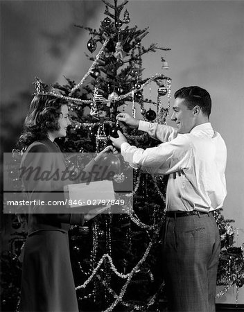 1940s COUPLE DECORATING CHRISTMAS TREE WITH CHRISTMAS BALLS