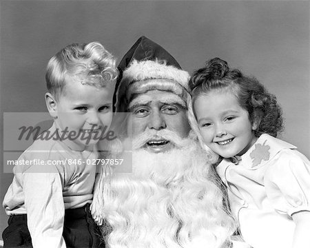 1940s MAN SANTA CLAUS POSING WITH YOUNG BOY AND GIRL IN LAP SMILING INDOOR