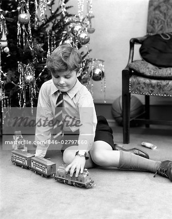 ANNÉES 1930 JEUNE GARÇON JOUANT AVEC TOY TRAIN DE SAPIN DE NOËL