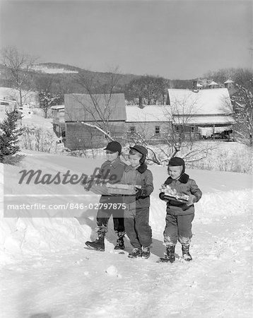 1950s 3 BOYS WALKING ON SNOW COVERED FIELD BY FARM EACH CARRYING GIFTS PRESENTS WINTER DRESS CHRISTMAS GIFT