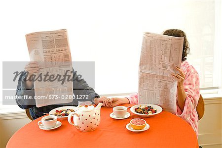 Couple having breakfast and reading newspaper together