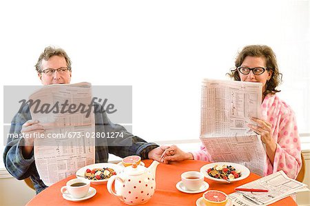 Couple having breakfast and reading newspaper together