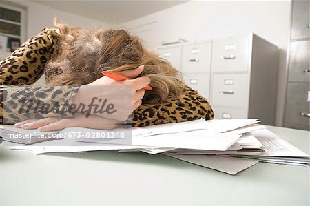 Woman resting head on table while writing checks