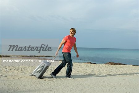 Man Pulling a Suitcase Across the Beach, Ibiza, Spain