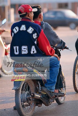 Jeune garçon en vêtements occidentaux, jeans et baseball cap sur l'arrière d'une moto à Vientiane, au Laos, Indochine, Asie du sud-est, Asie