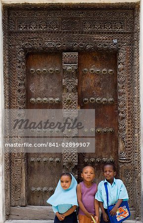 Three children sitting in front of a carved wooden Arab door in Stone Town, Zanzibar, Tanzania, East Africa