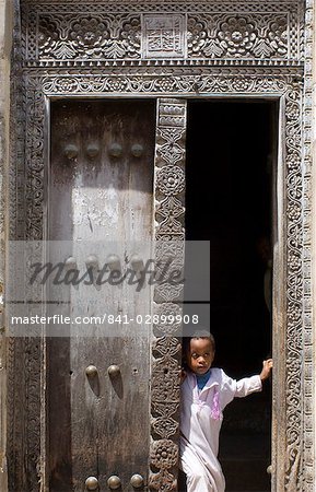 Jeune garçon à la recherche d'une porte arabe en bois sculptée traditionnelle à Stone Town, Zanzibar, Tanzanie, Afrique de l'est