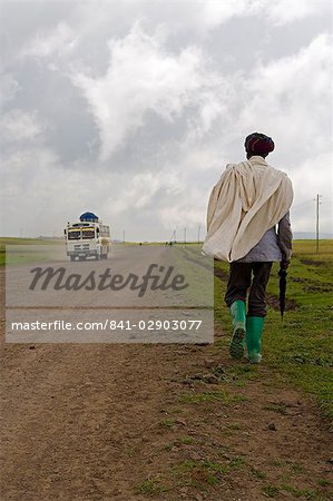 Homme marchant le long de la bottes de route pendant la saison des pluies port vert et tenant un parapluie, les hauts plateaux éthiopiens, Ethiopie, Afrique