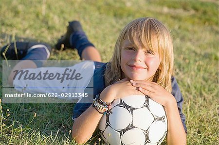 Junge lächelnd und mit Fußball auf Gras liegend